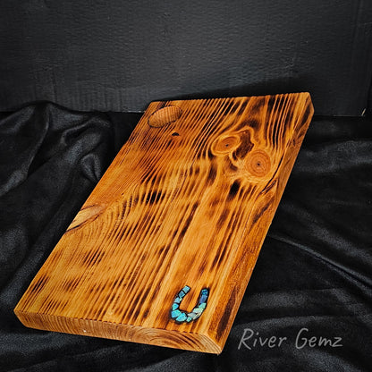Wooden cutting board with a blue horseshoe on a black fabric background, branded 'River Gemz'.