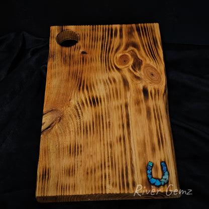 Wooden cheese board with a blue and green horseshoe charm on a black background