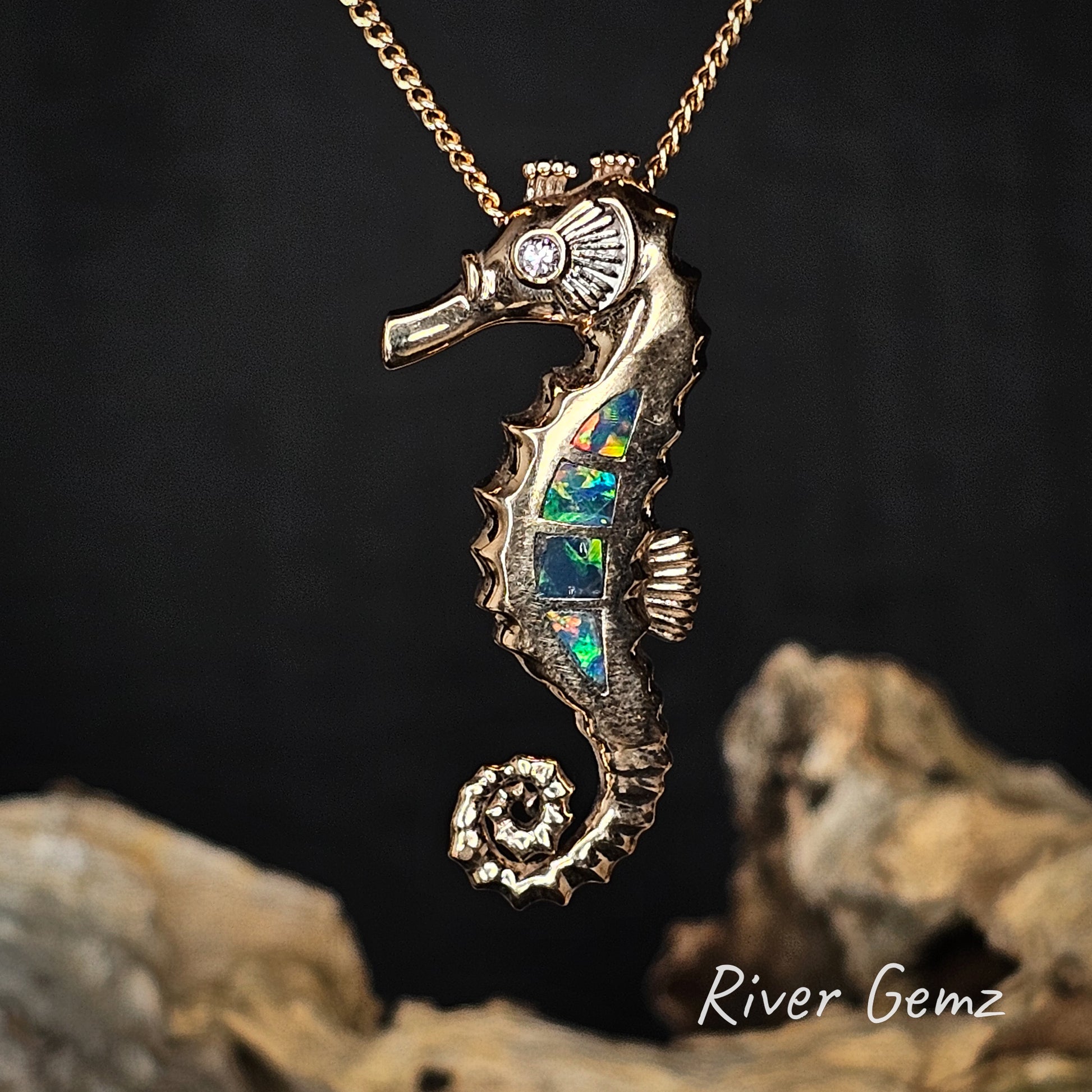 Gold seahorse pendant with colourful opal inlay on a chain against a dark background