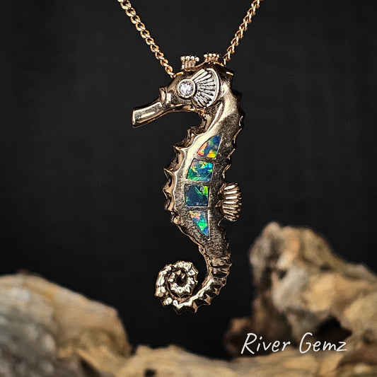 Gold seahorse pendant with colourful opal inlay on a chain against a dark background