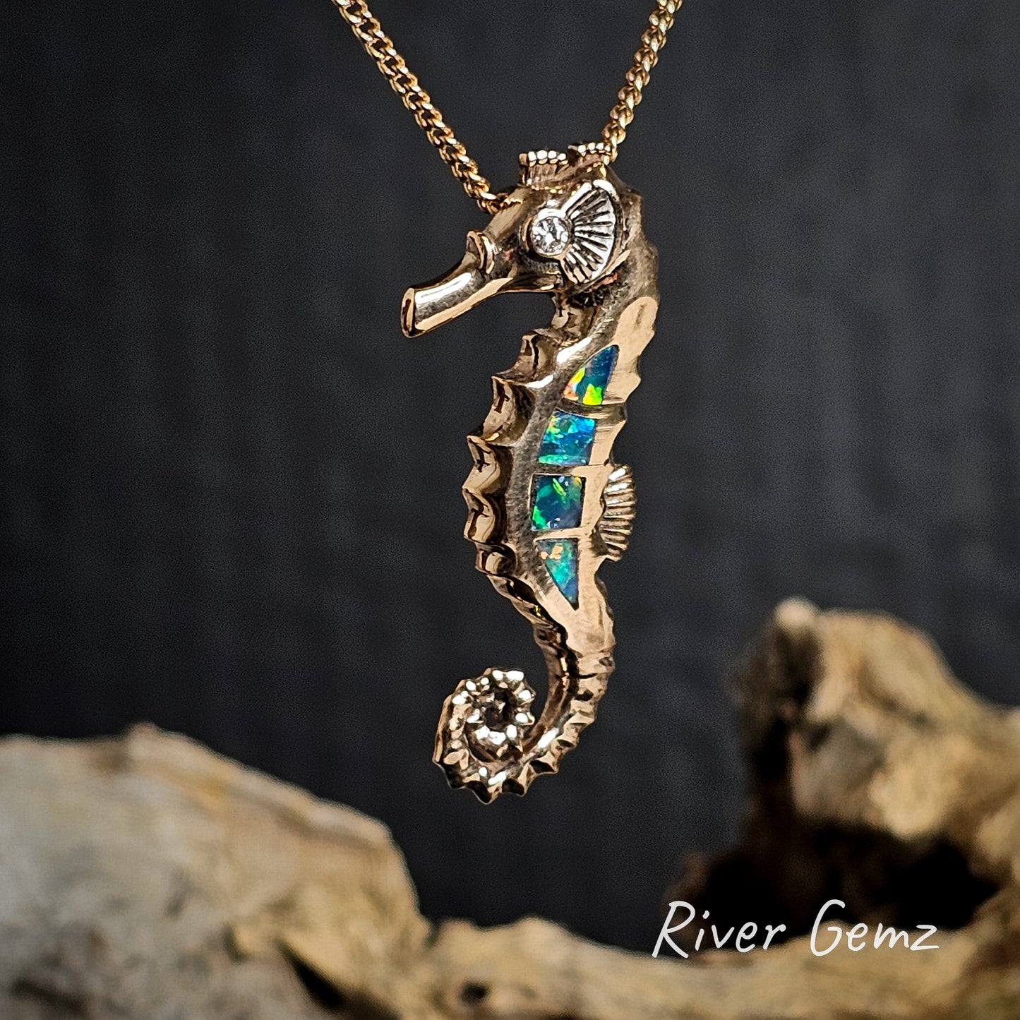 Gold seahorse pendant with 4 multi-coloured crystal opals and a diamond on a chain against a dark background