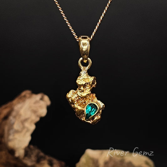Natural gold nugget and emerald stone set in yellow gold pendant against a dark background.