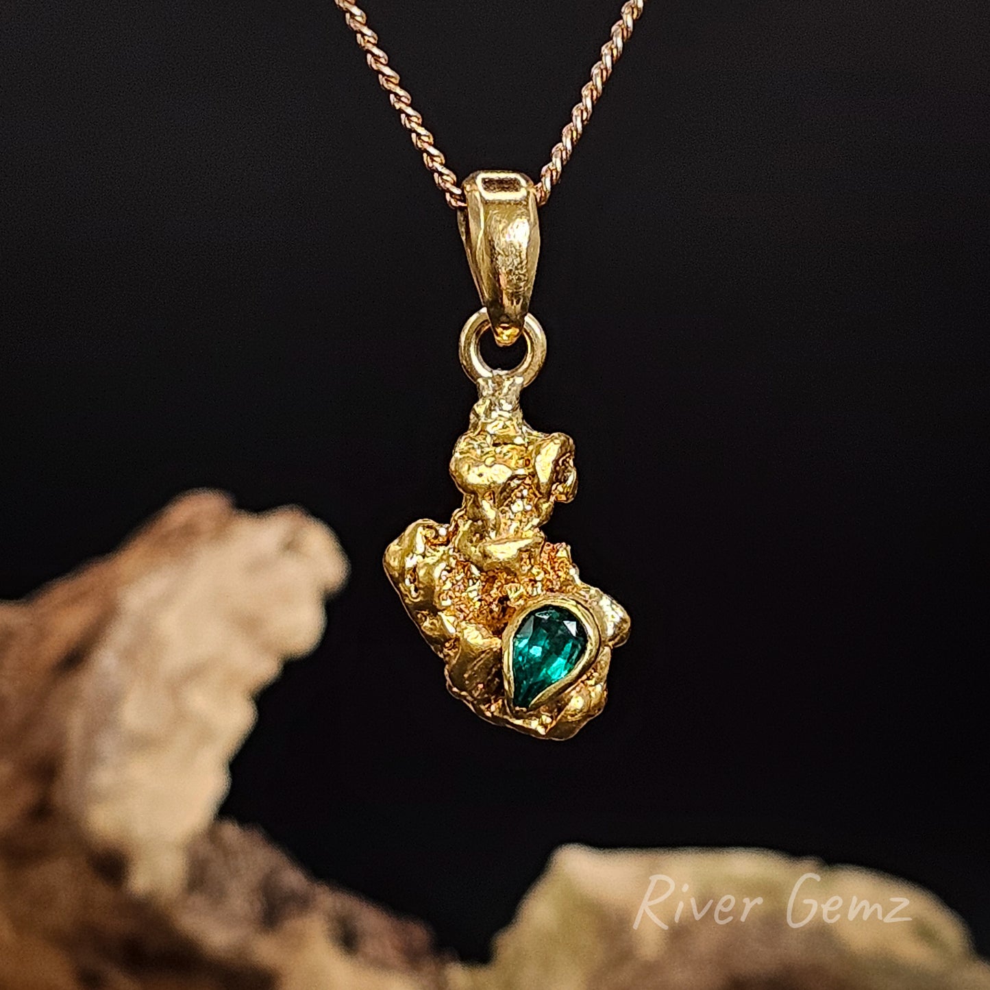 Yellow nugget and green emerald stone in a pendant against a black background. 