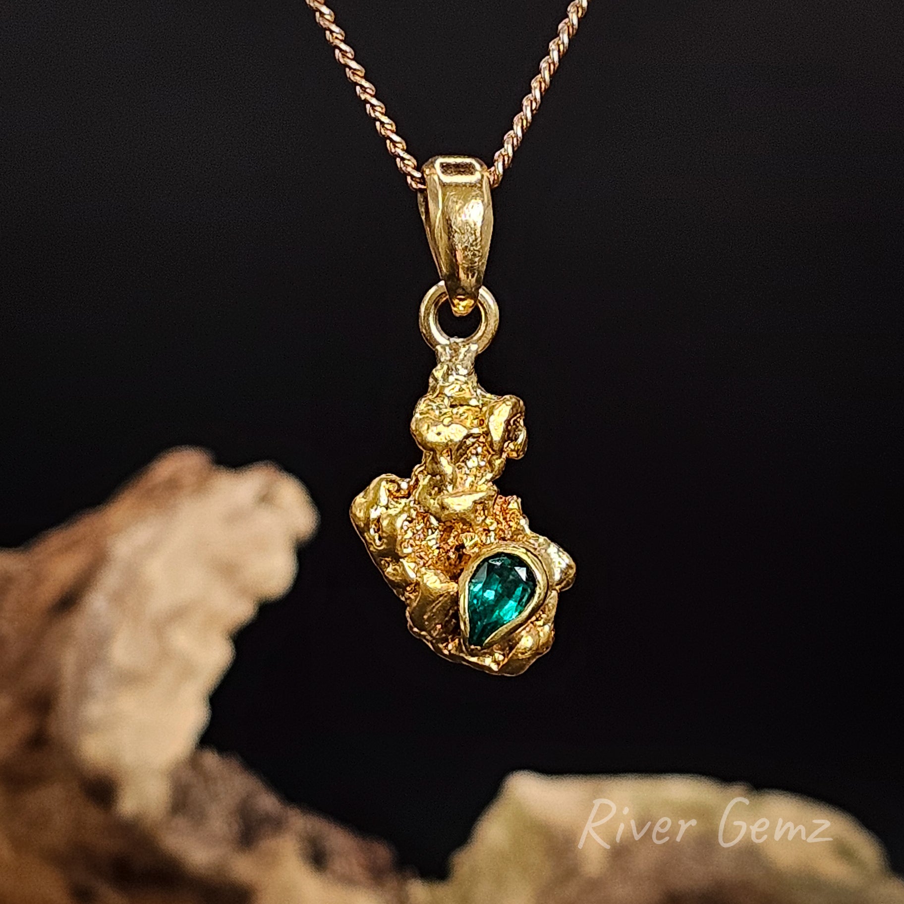 Yellow nugget and green emerald stone in a pendant against a black background. 