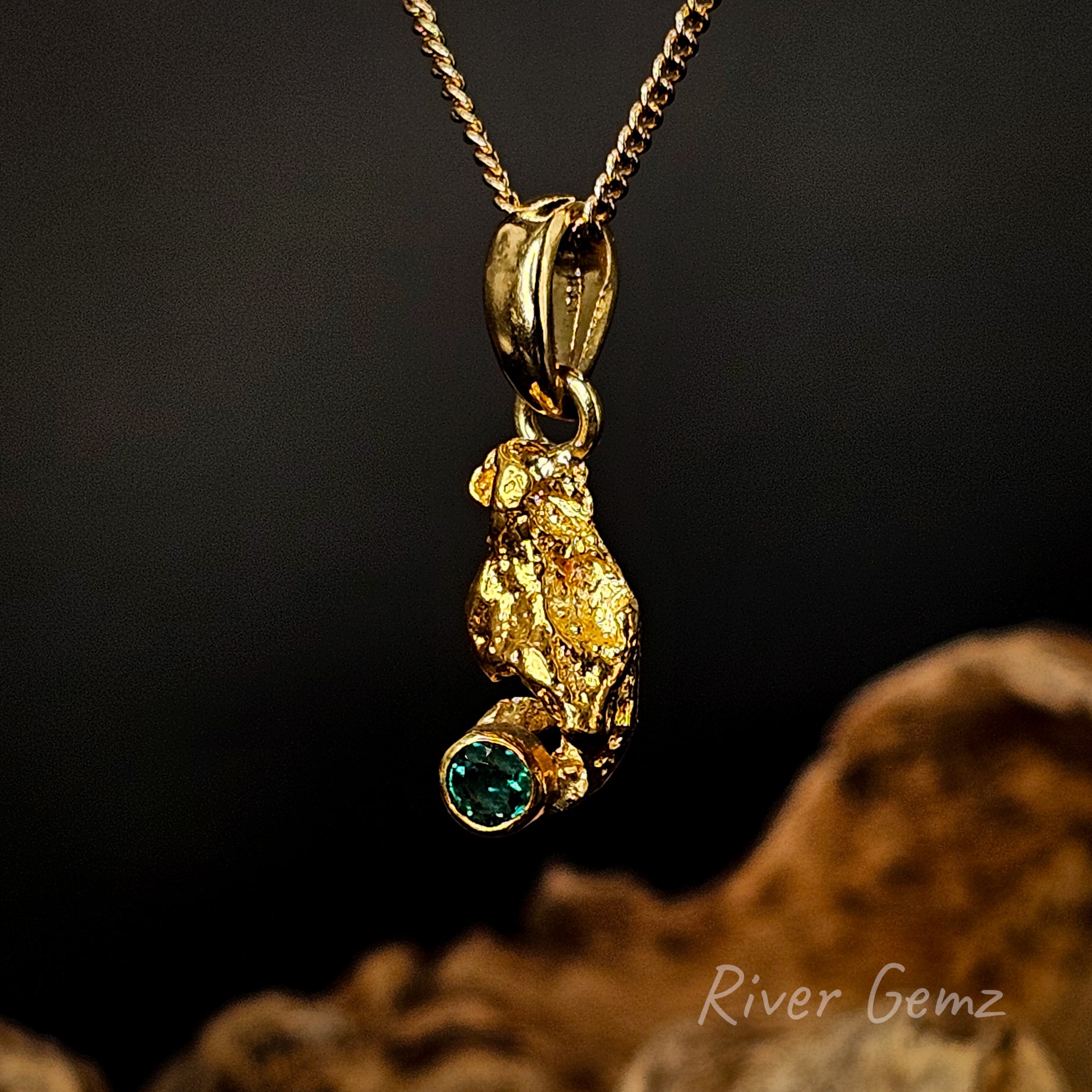 Natural gold nugget and besel set round emerald in an 18K yellow gold pendant against a dark background.