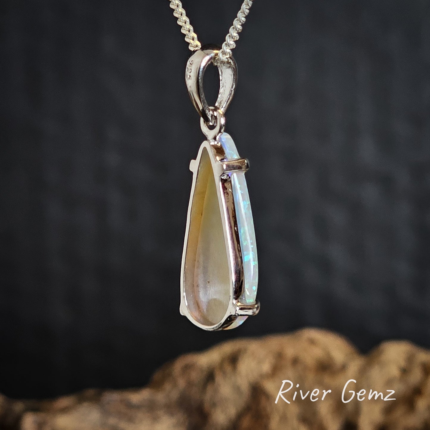 Side/rear view of teardrop-shaped opal pendant on a chain with a dark background, featuring 'River Gemz' branding.