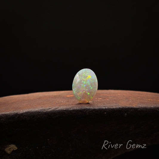 Oval shaped light opal stone on a dark surface with 'River Gemz' branding.