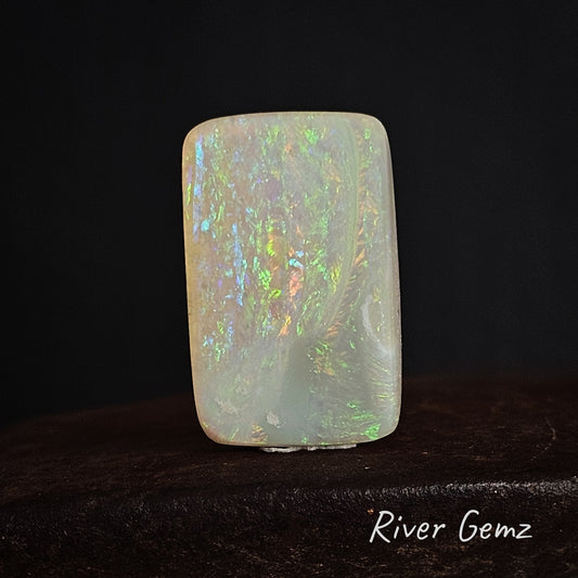 Opal stone with multicolored play of colours on a dark background, branded 'River Gemz'.