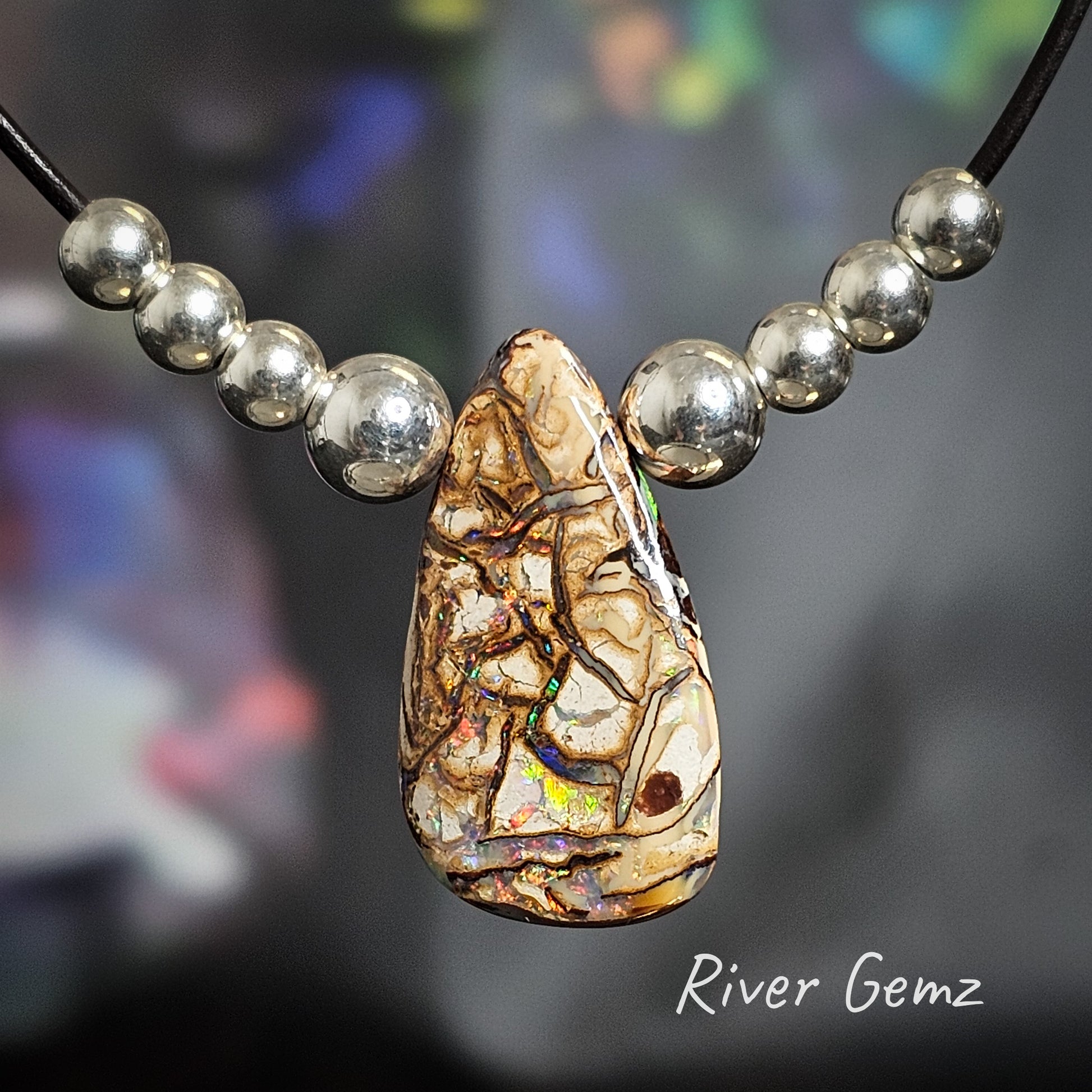 Teardrop shaped light brown coloured opal with multi-coloured veins throughout with 4 silver beads each side on a leather necklace.