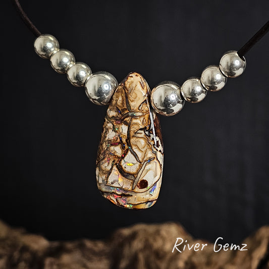 Necklace with a decorative pendant and silver beads on a dark background, featuring 'River Gemz' branding.
