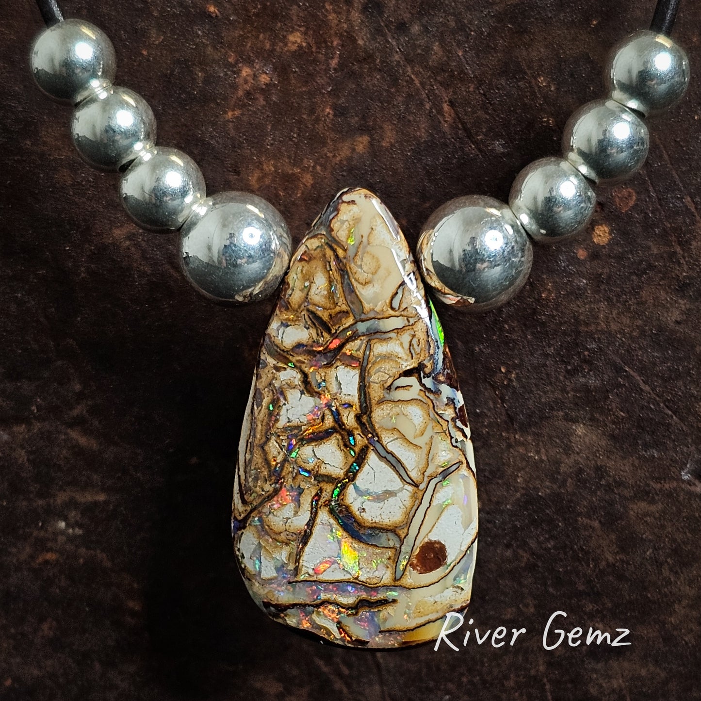 Rounded triangular shaped earth-toned boulder opal with multiple beads each side of the feature stone in a leather necklace.