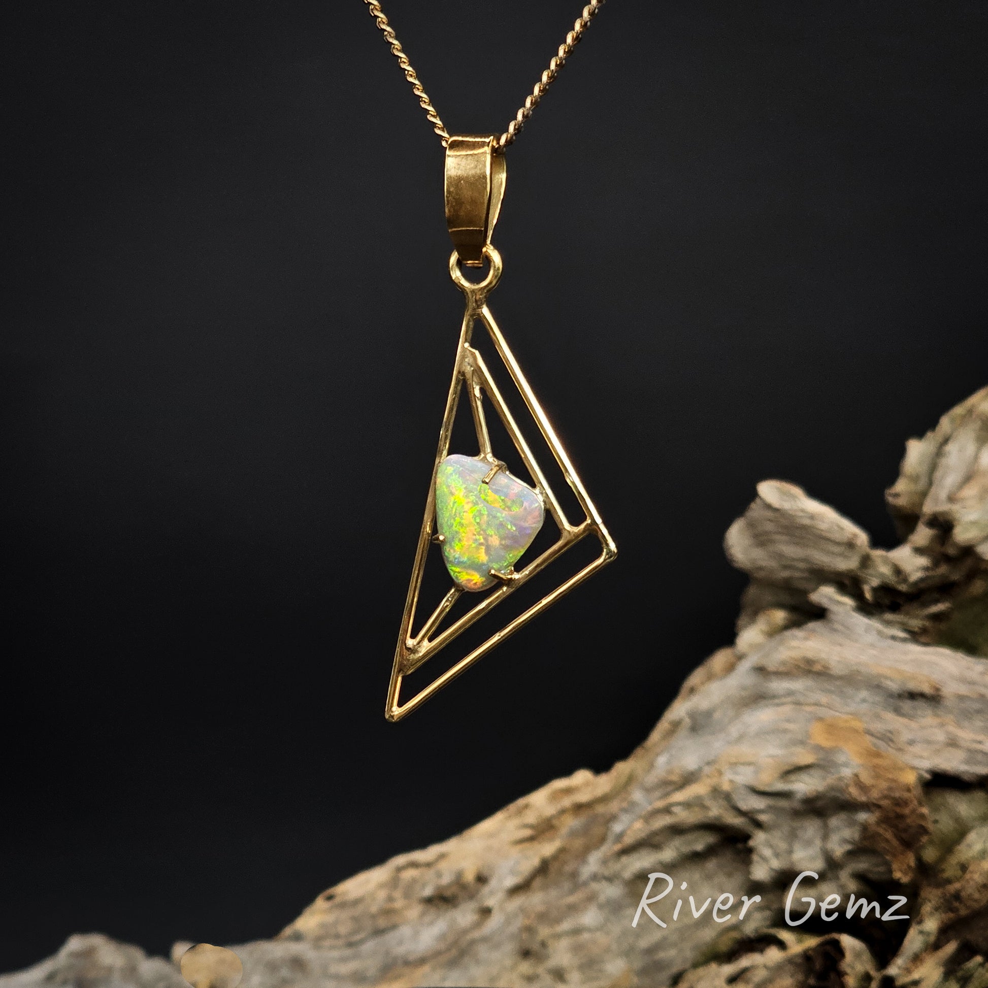Gold pendant with a triangular design and yellow and green opal stone on a dark background