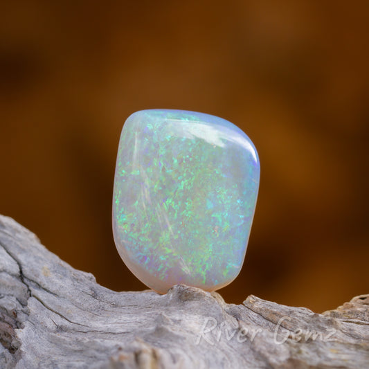 Large 4 sided blue-green unset light opal standing on light grey drift wood.