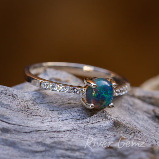 Round black opal and multi topaz silver ring laying on light grey textured wood.