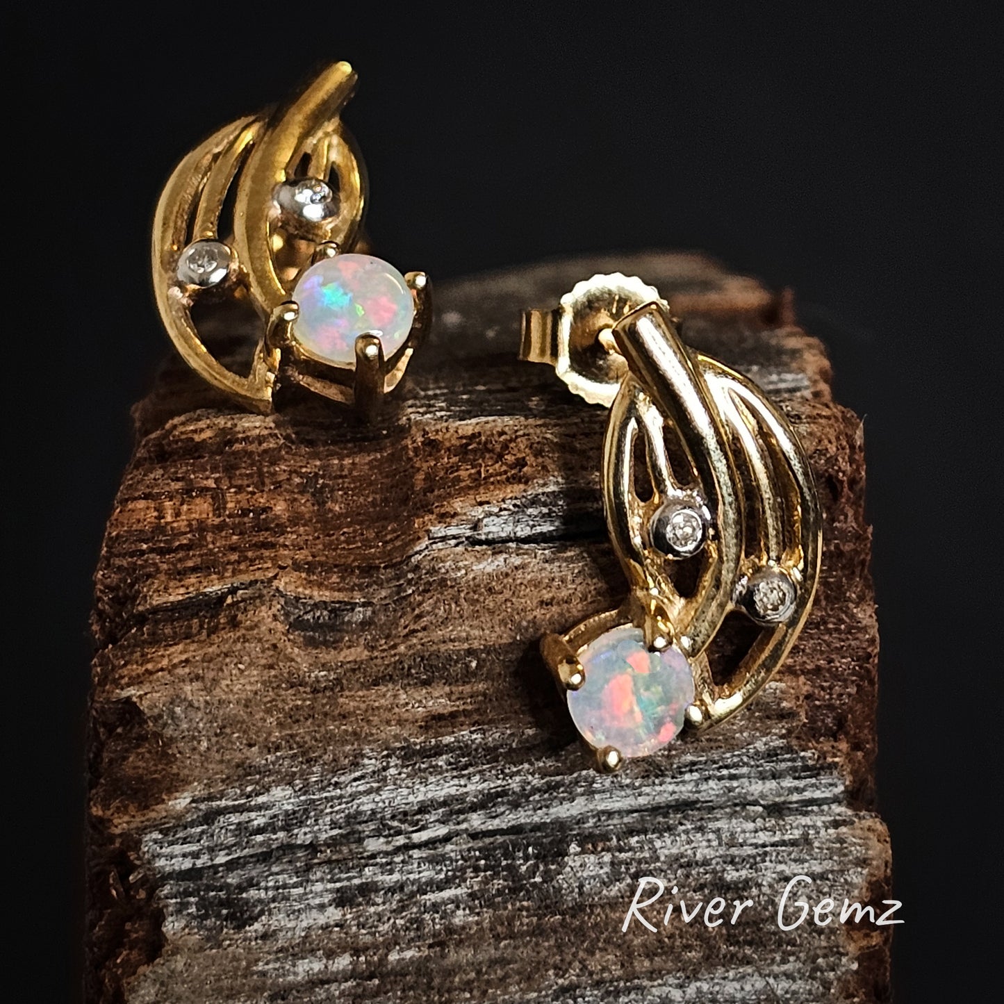 Gold earrings with opal stones and diamonds on a wooden block, branded 'River Gemz'.