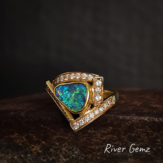 Gold ring with heart-shaped opal stone and diamond accents on a dark background, branded 'River Gemz'.