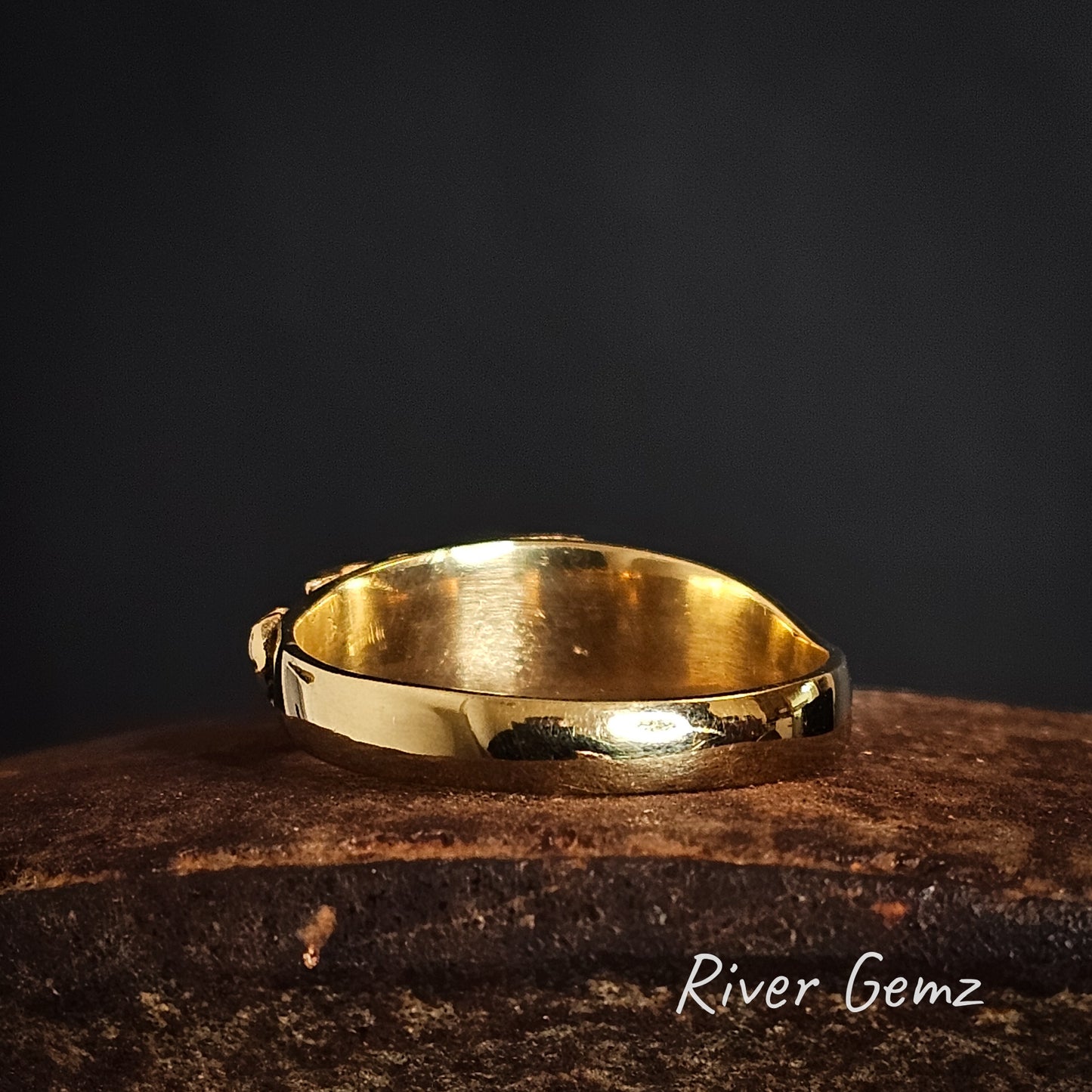 Back of gold ring on a dark surface with 'River Gemz' branding.
