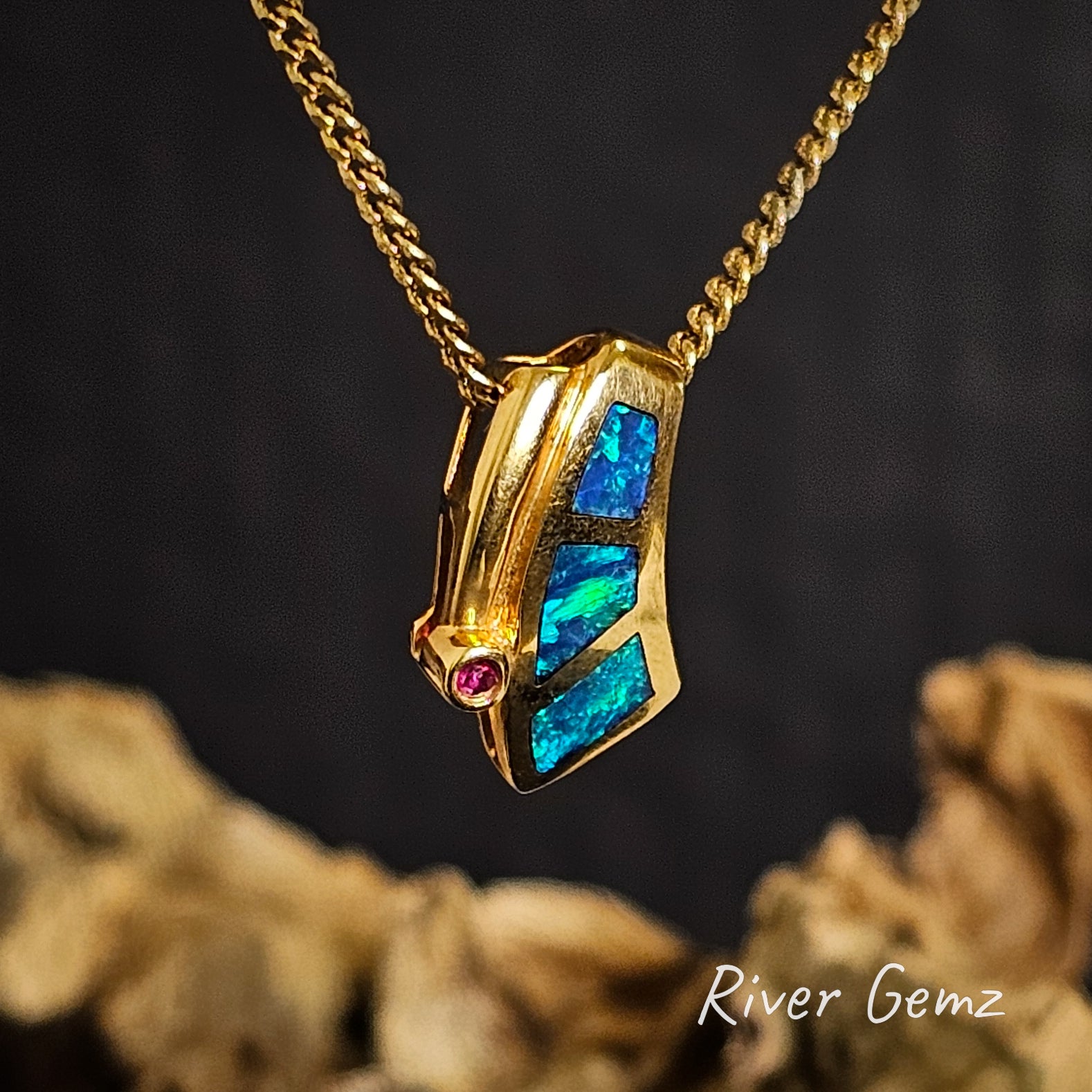 Gold necklace with three irregular shaped opals on a dark background branded 'River Gemz'.