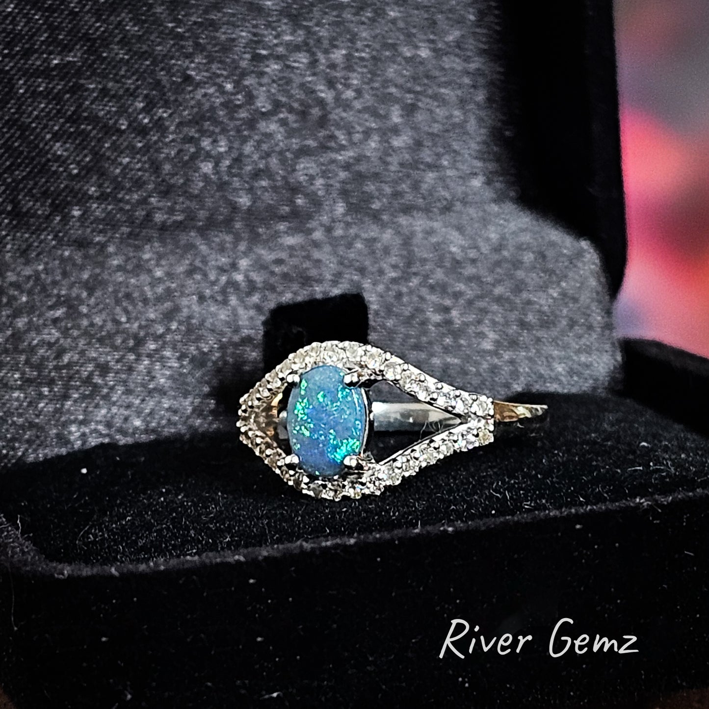 Eye shaped ring with opal pupil and white topaz outline shown in black velvet ring box.