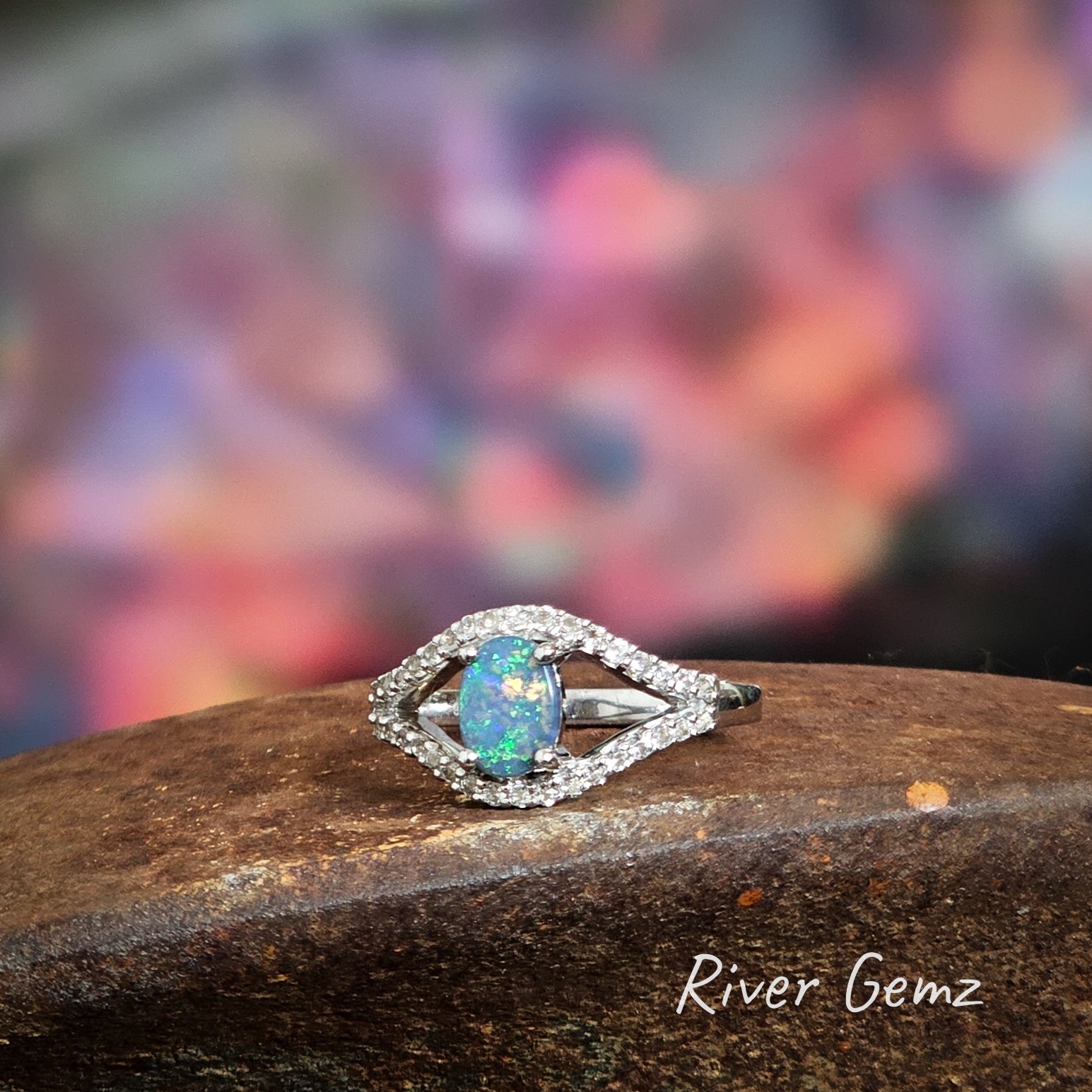 Green and blue oval shaped black opal claw set in sterling silver ring with white topaz surrounds.