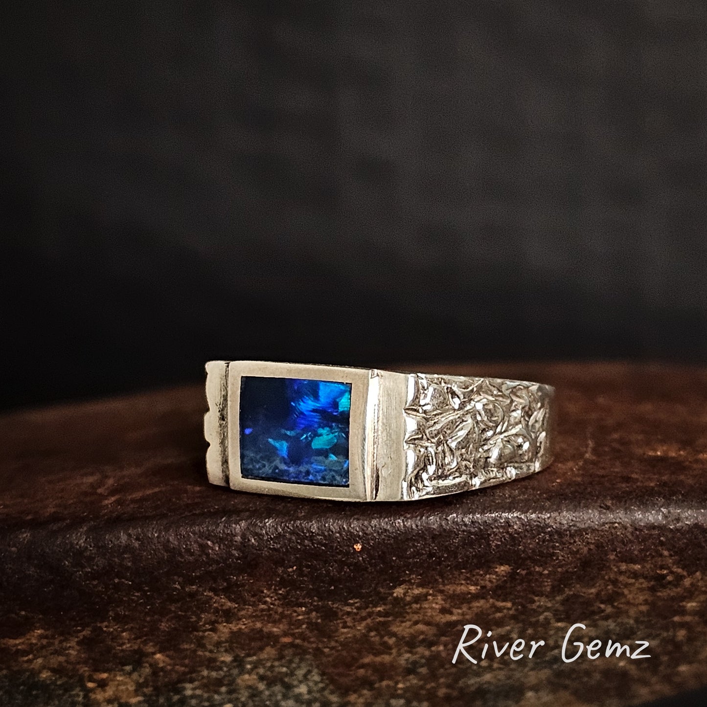 Silver ring with rectangular shaped blue dark opal on a dark background, featuring 'River Gemz' branding.