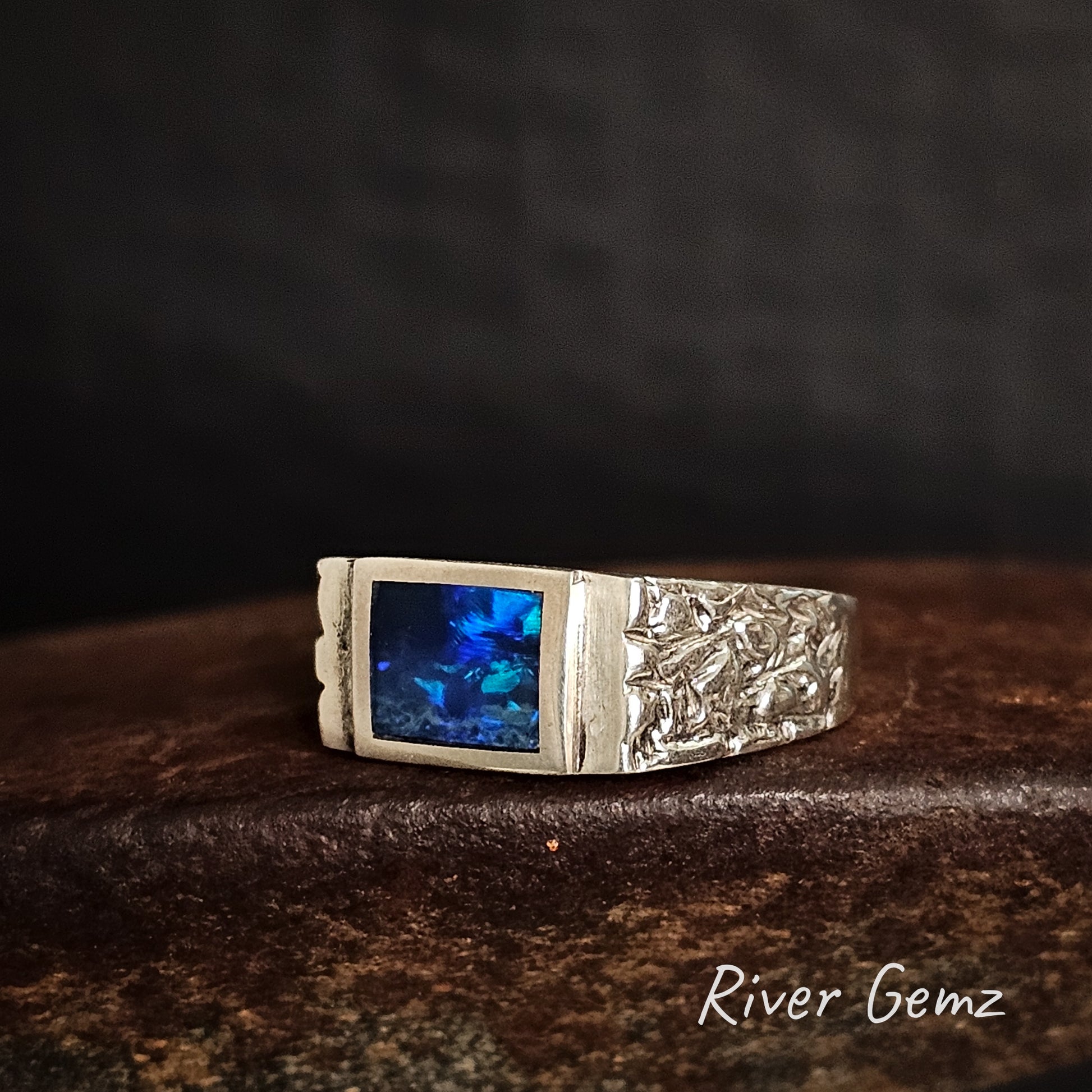 Silver ring with rectangular shaped blue dark opal on a dark background, featuring 'River Gemz' branding.