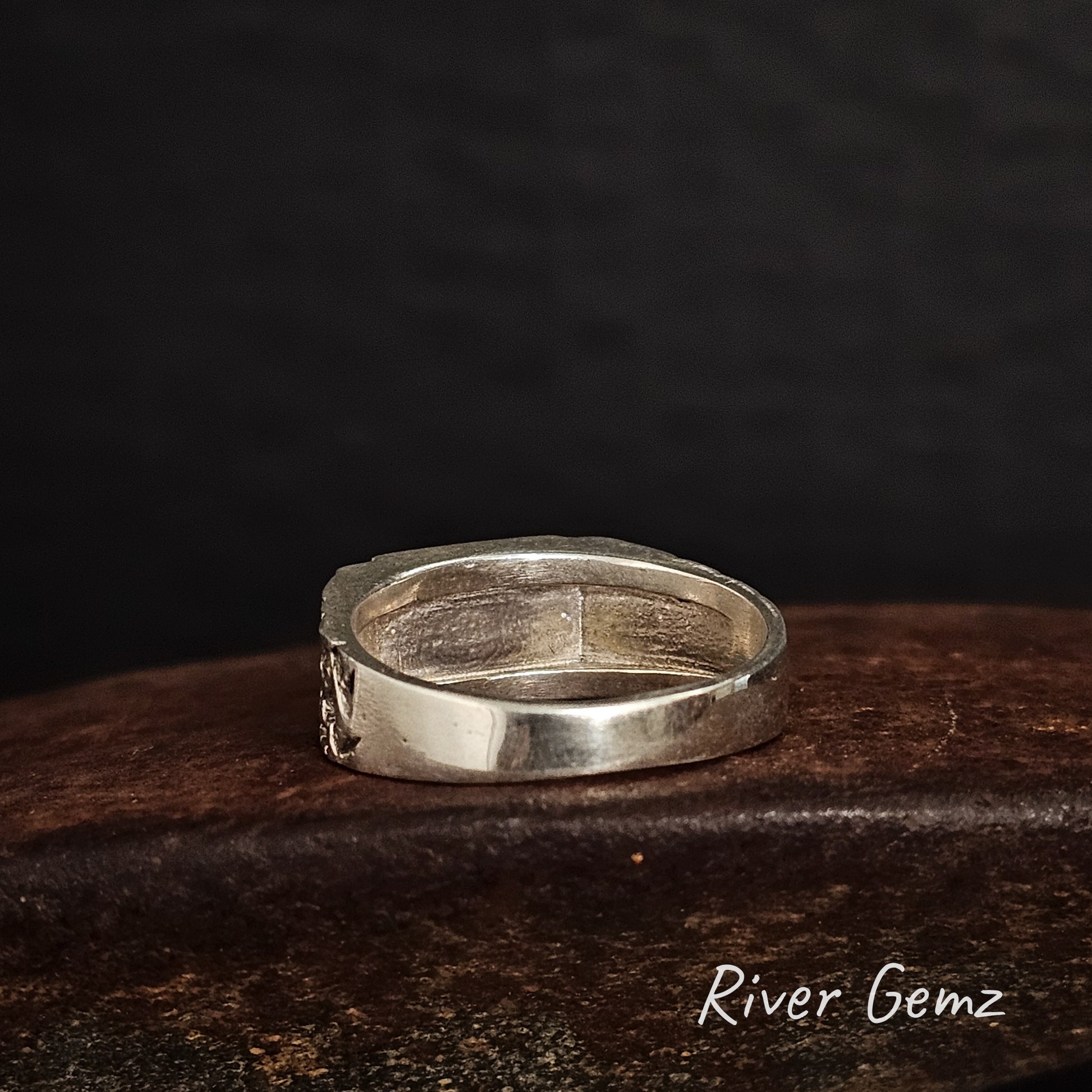 Back of ring showing the silver behind the inlaid opal on a cast iron surface with 'River Gemz' branding.