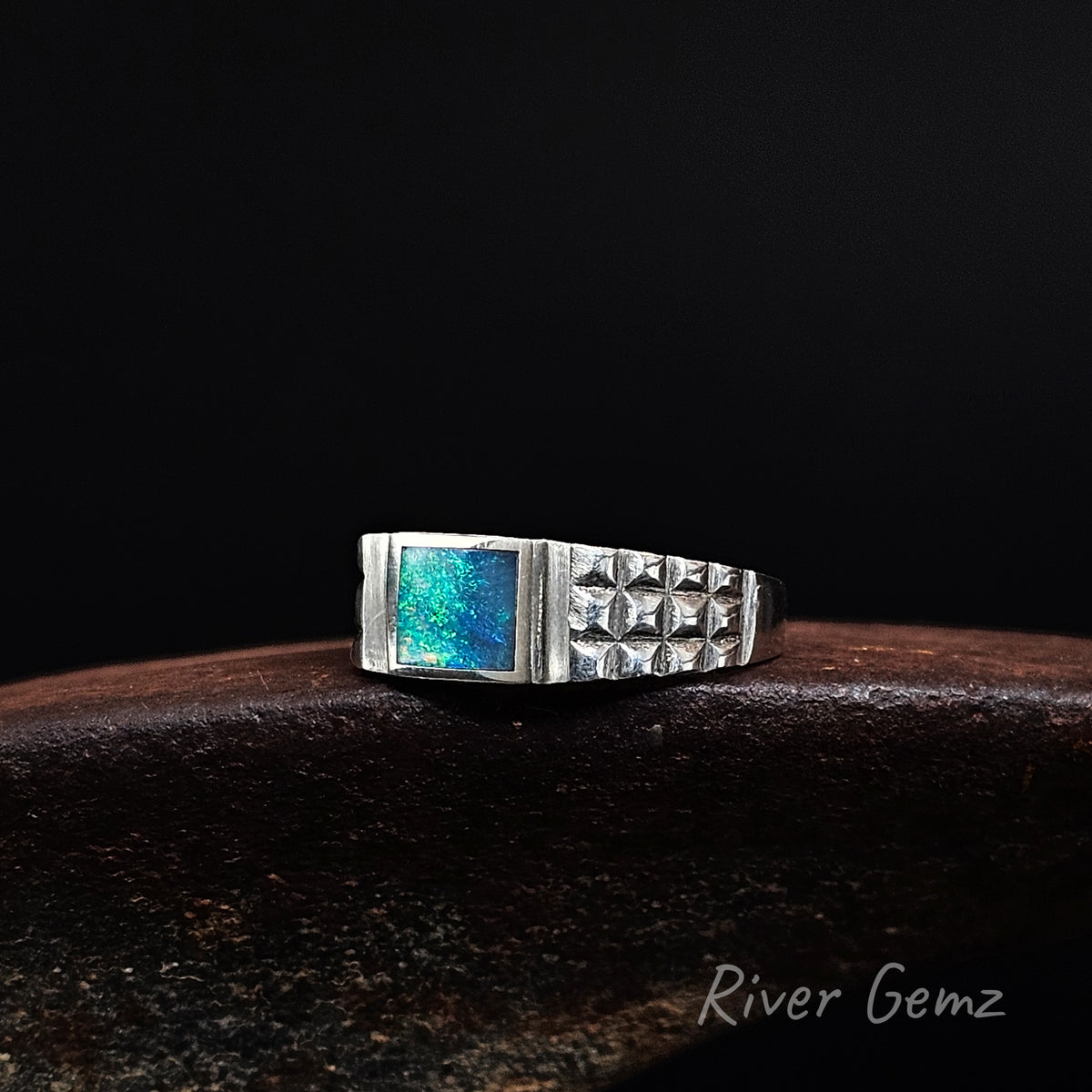 Rectangular shaped blue and green opal in a silver ring with chequered pattern pressed into the shoulders.