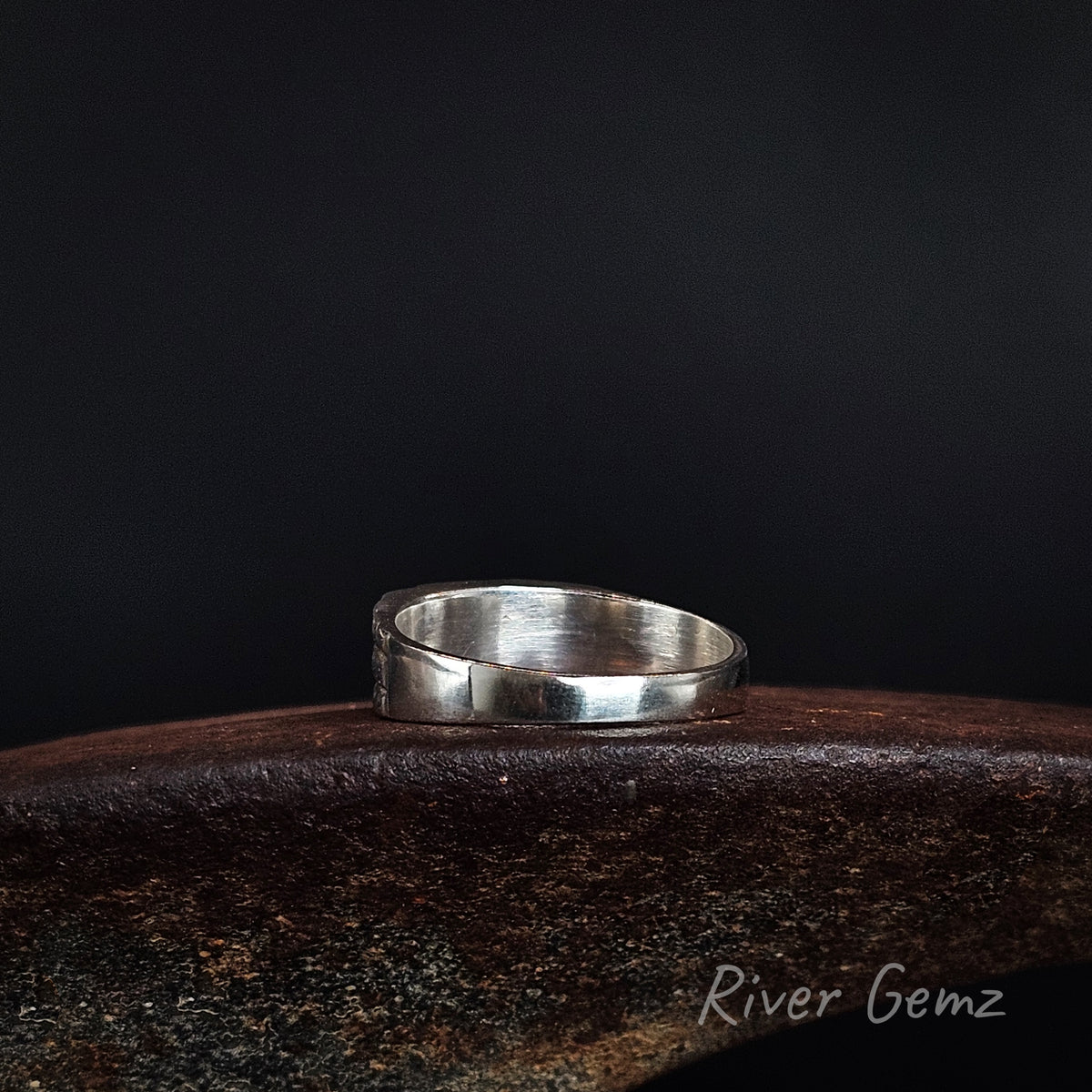 Rear view of ring shows the full silver cover behind the opals on a weathered shoe anvil and black background with 'River Gemz' watermark.