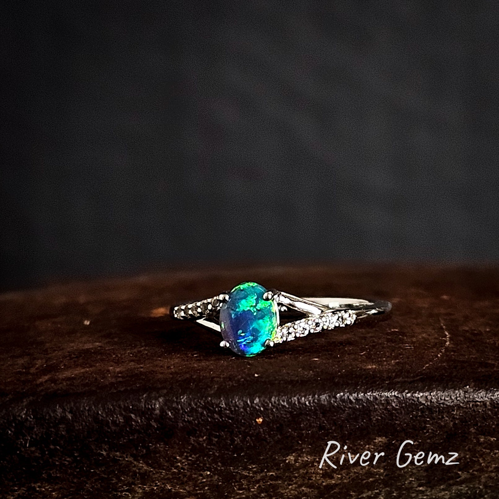 Ring with a oval-shaped dark blue/green gemstone on a dark background, branded 'River Gemz'.