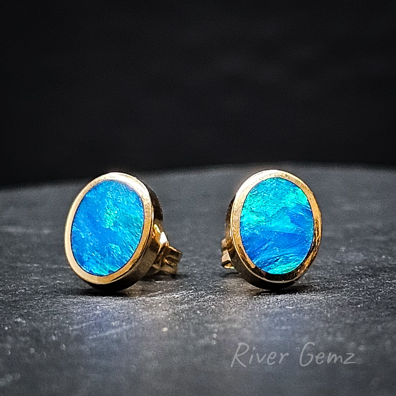 Vivid blue and green dark opals in yellow gold earrings pictured with black surrounds.