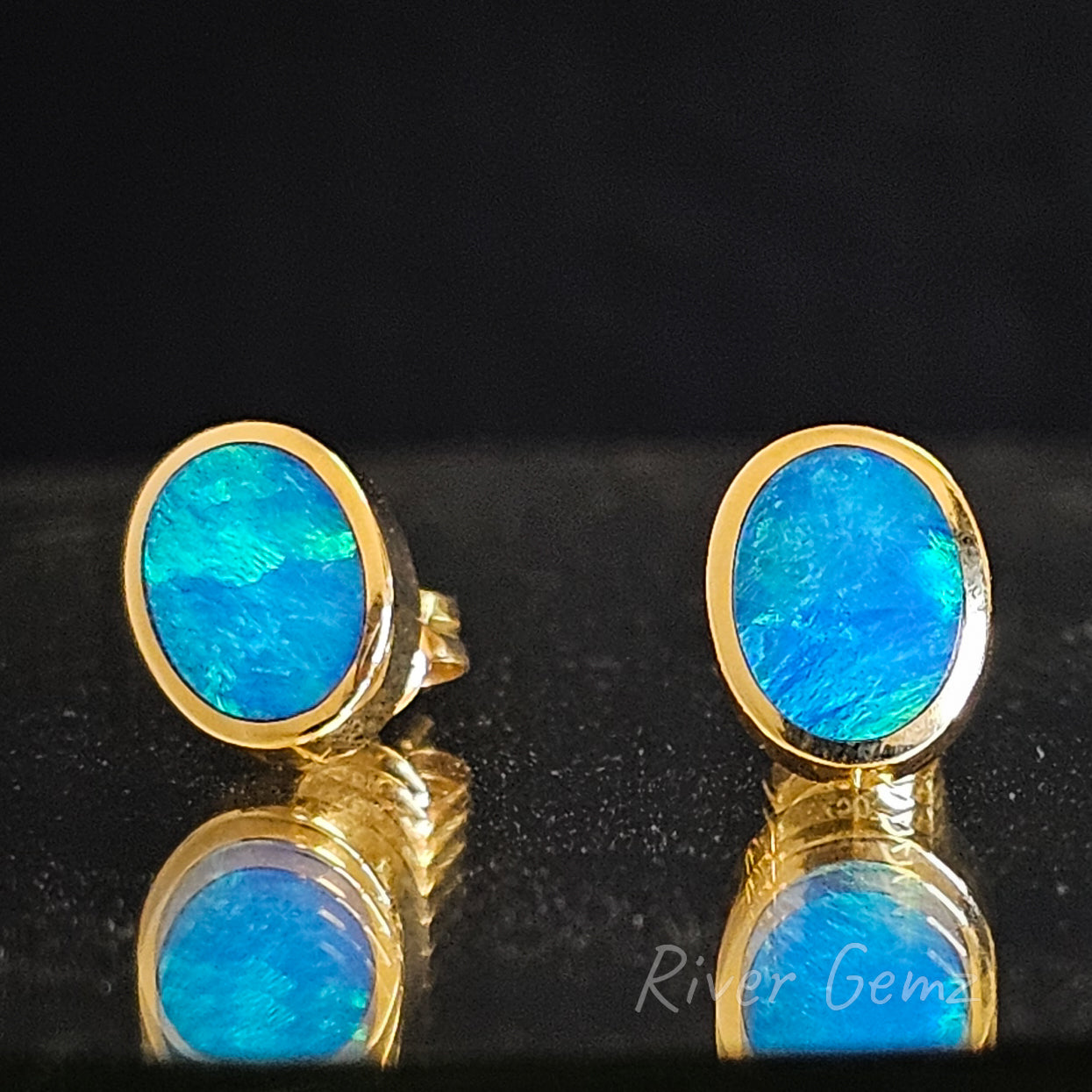 Oval shaped earrings photographed on reflective surface.