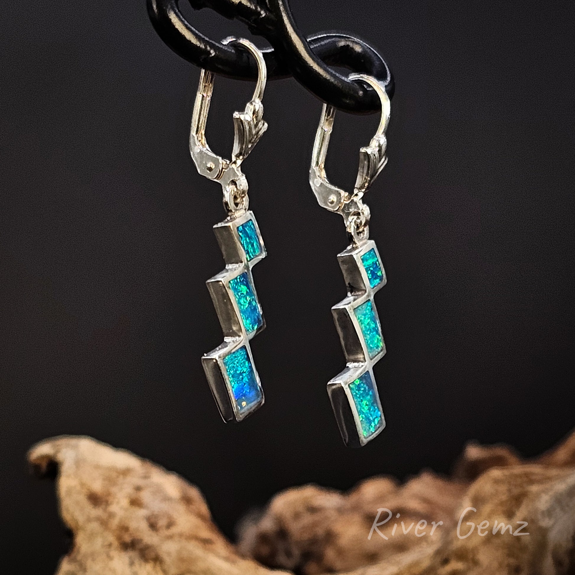 Pair of silver earrings with 3 blue opals on a dark background
