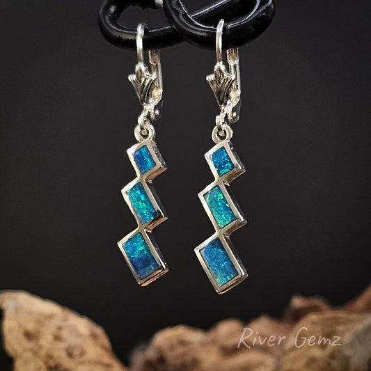 Pair of blue and green opals set in sterling silver earrings on a dark background with 'River Gemz' branding.