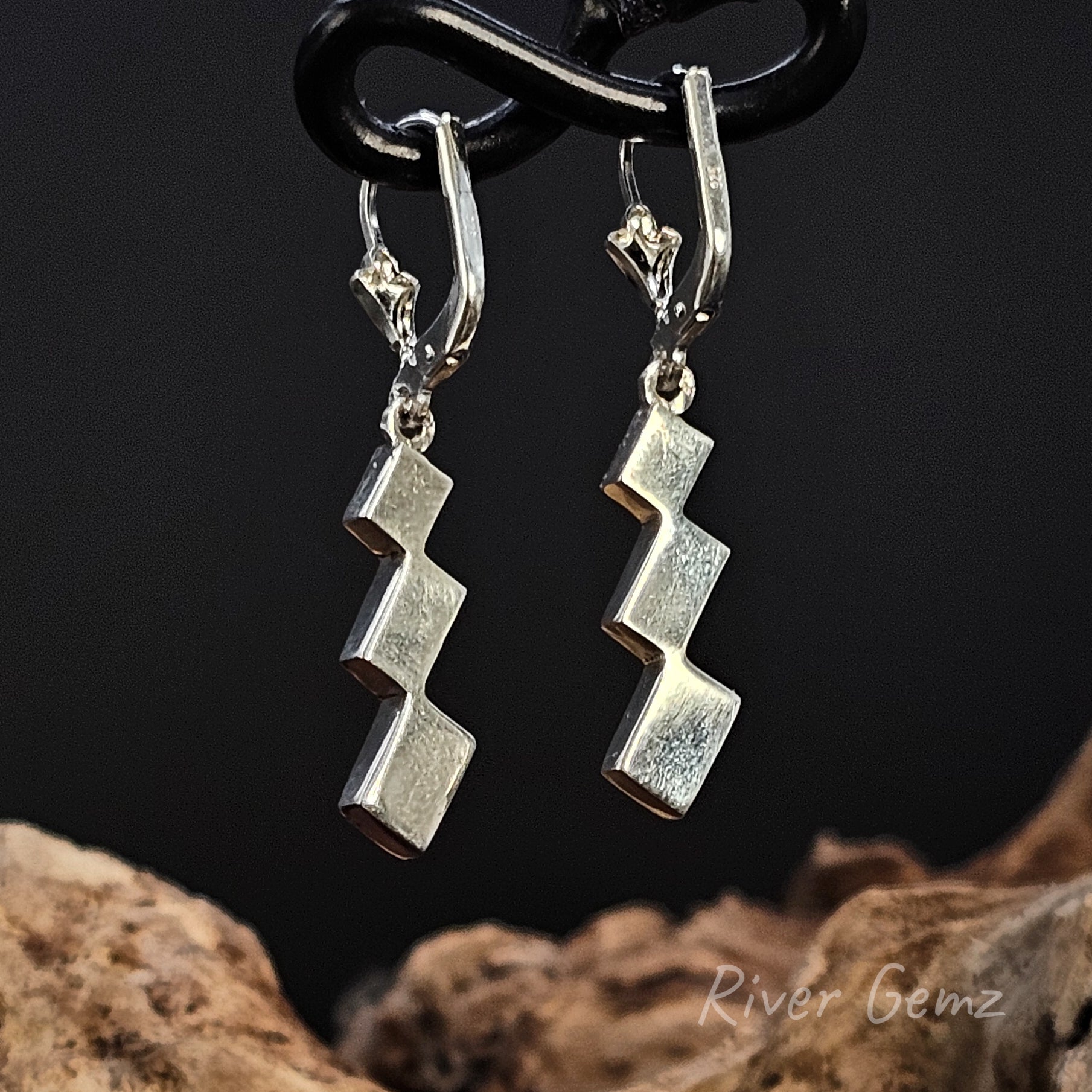 Rear view of silver zigzag earrings on a dark background with 'River Gemz' branding.
