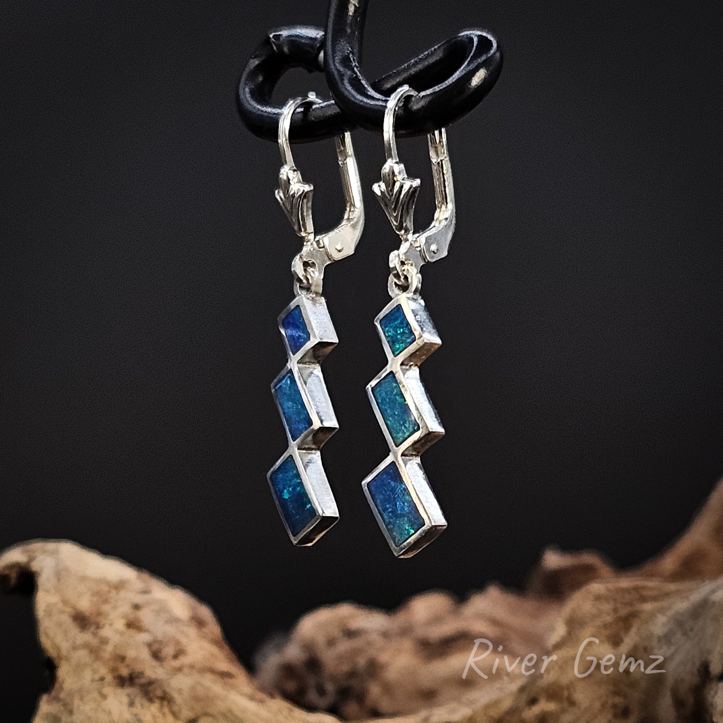 Pair of blue and silver earrings on a black stand with a natural wood background