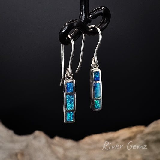 Pair of blue and green opal hook earrings on a black background with 'River Gemz' branding.