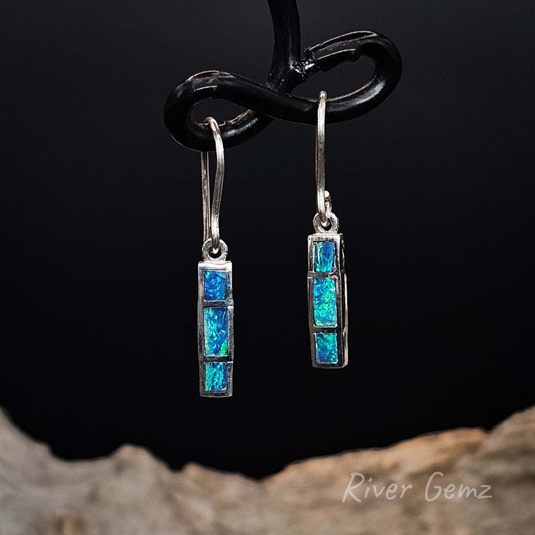 Pair of silver earrings with 3 rectangular shaped blue dark opals on a black background