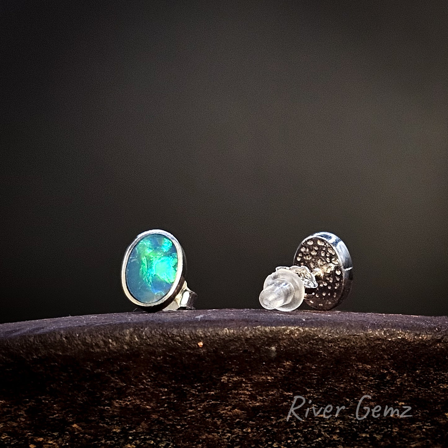 Pair of sterling silver studs with blue and green opals on a dark surface with a black background, featuring 'River Gemz' branding.