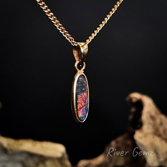 Gold necklace with a pendant featuring a colorful stone, set against a dark background.