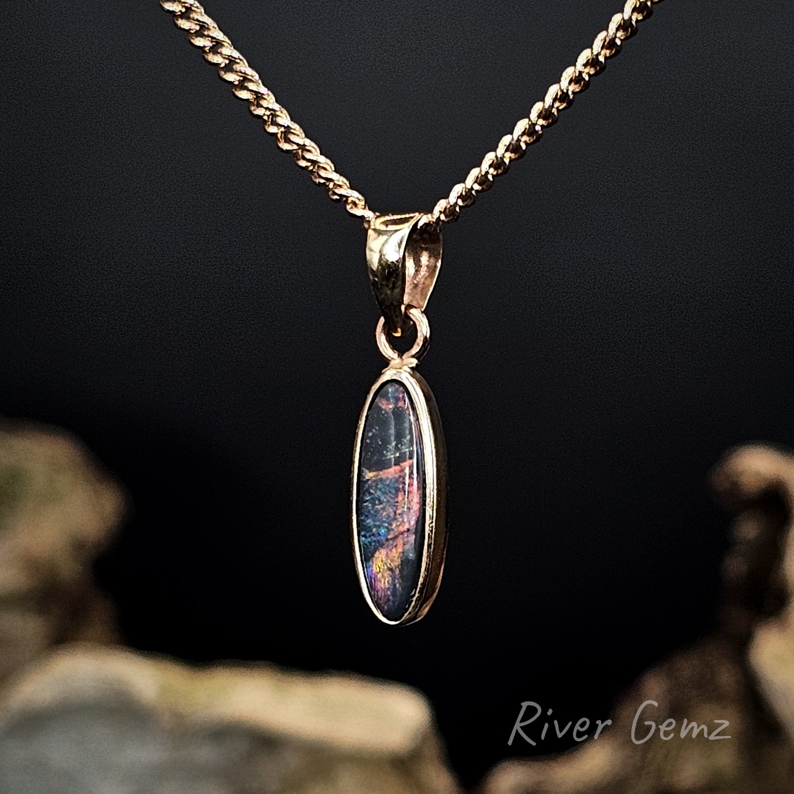 Gold pendant with an oval multi-coloured black opal on a chain against a dark background
