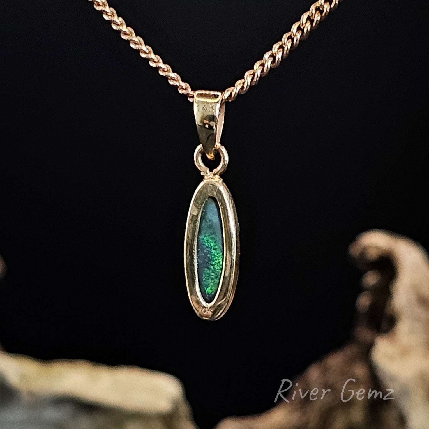 Rear view of gold pendant showing the dark base tone with a green tinge of the black opal on a dark background