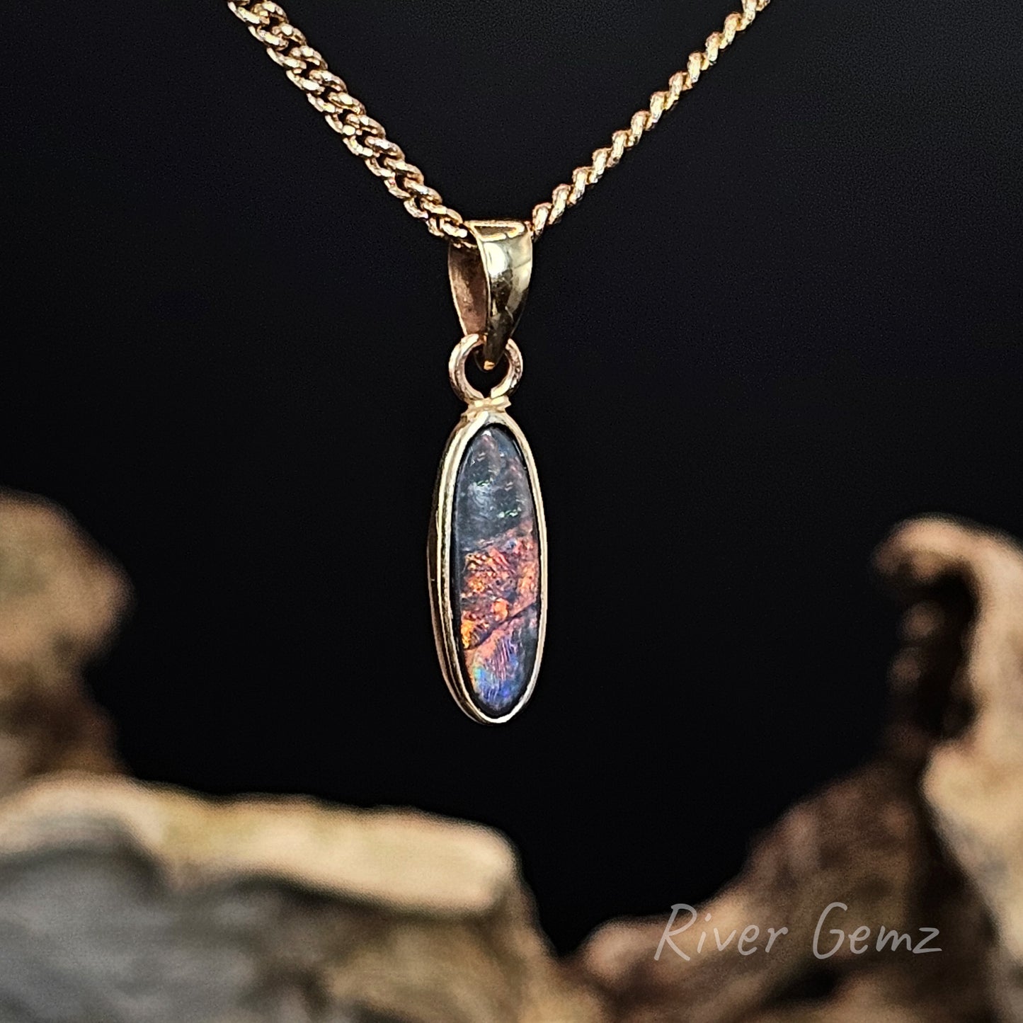 Gold pendant with a colourful stone on a dark background