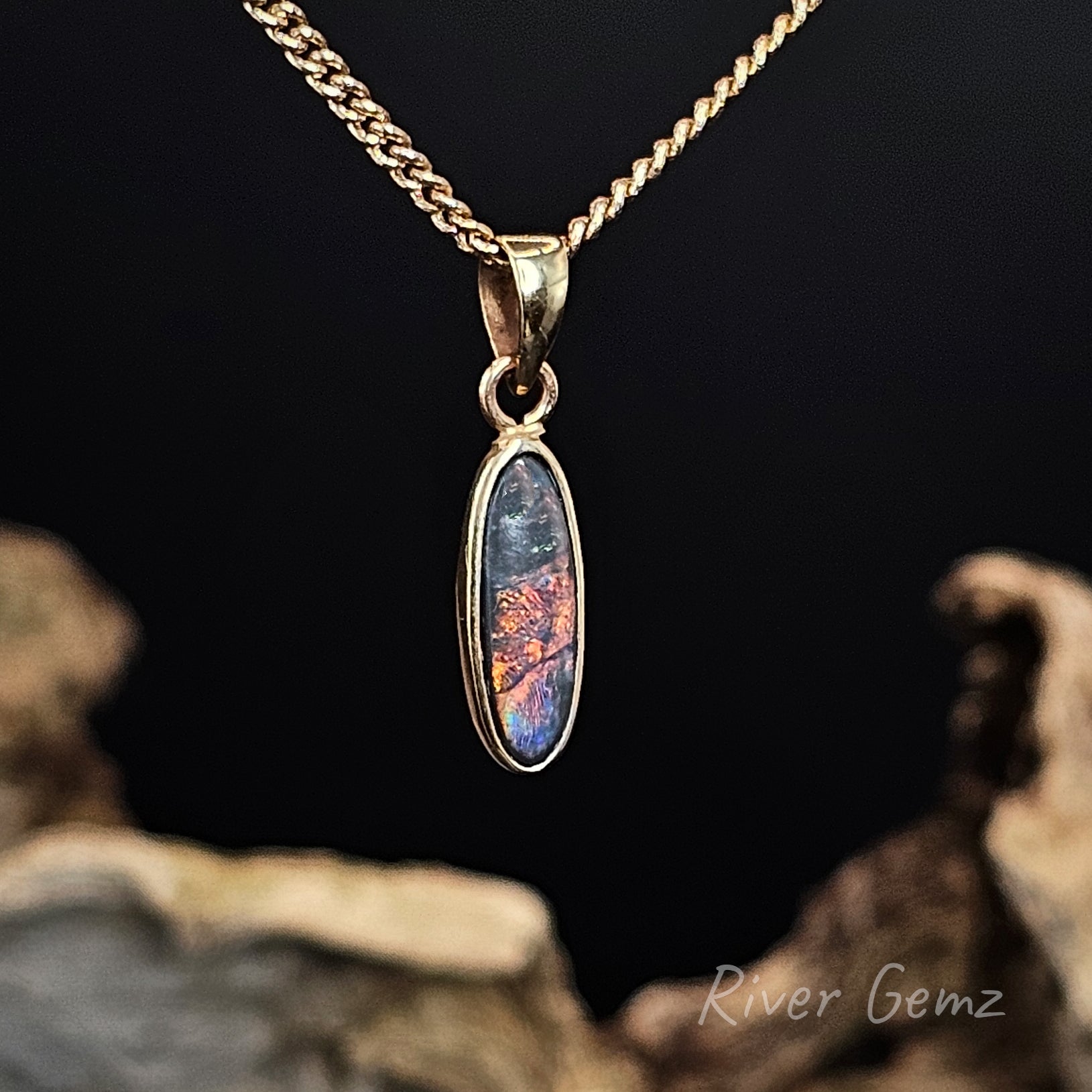 Gold pendant with a colourful stone on a dark background