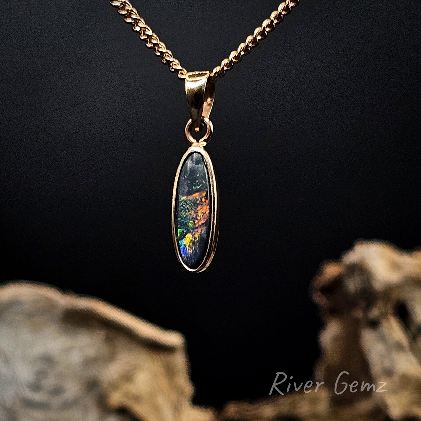 Gold necklace with a colorful pendant against a dark background