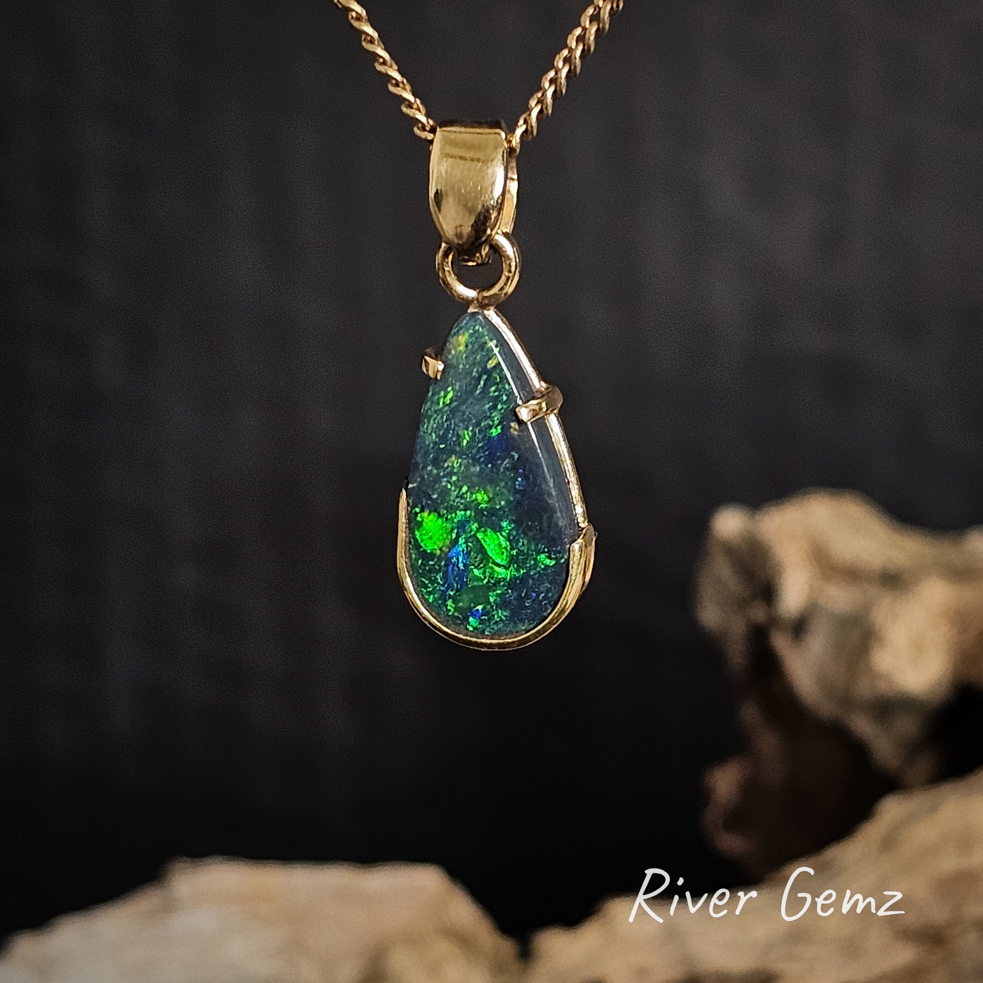 Teardrop-shaped opal pendant with gold setting on a dark background, featuring 'River Gemz' branding.