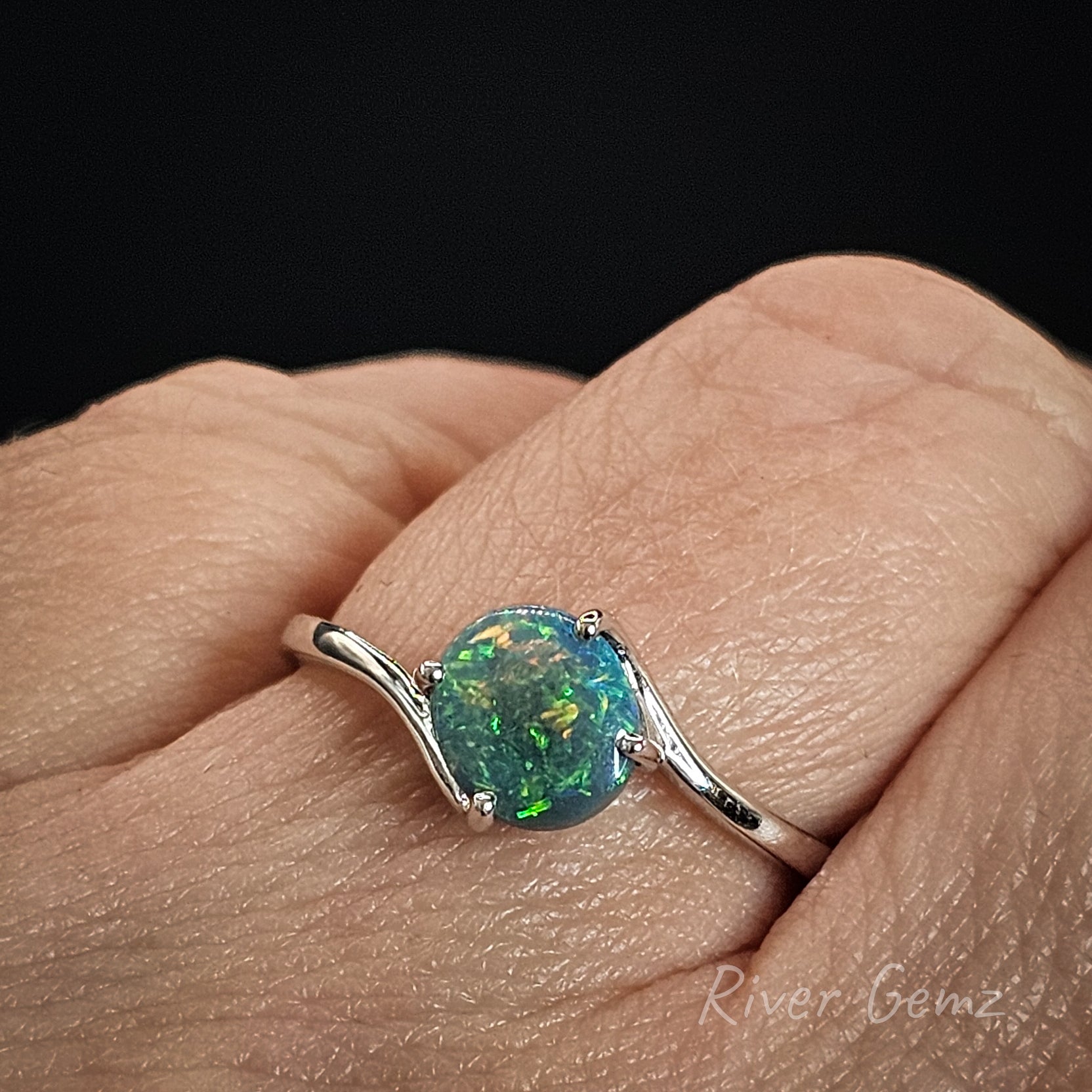 Opal ring on a hand with a black background.