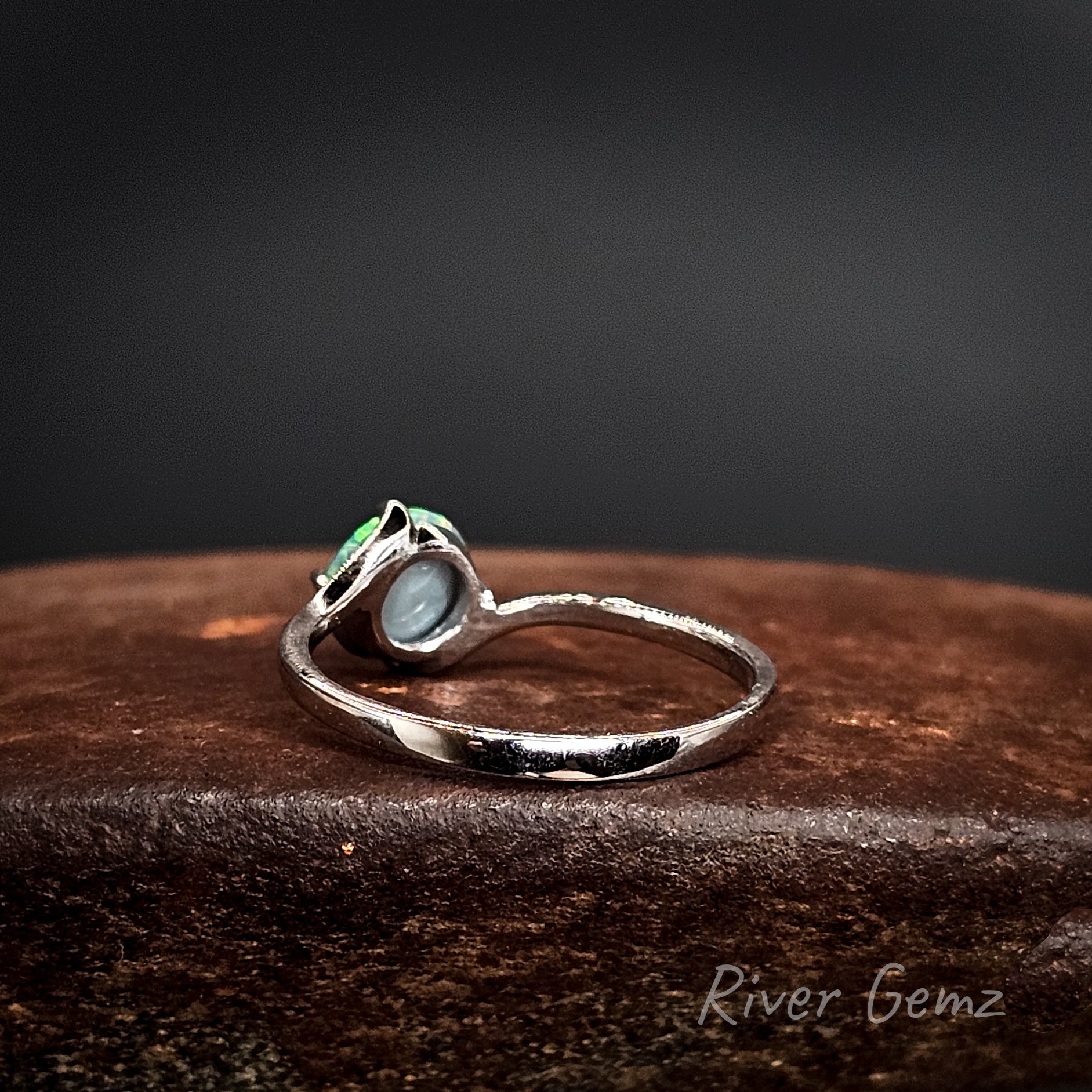 Rear view shows the dark base tone of the black opal set in the white gold ring on a dark surface, featuring 'River Gemz' branding.