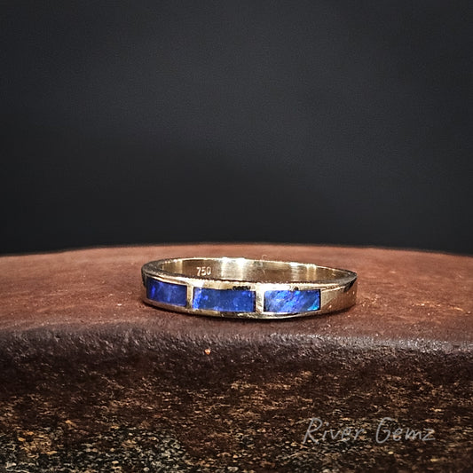 White gold ring with 3 blue dark opals on a dark surface. 750 stamp visible to indicate 18K gold.