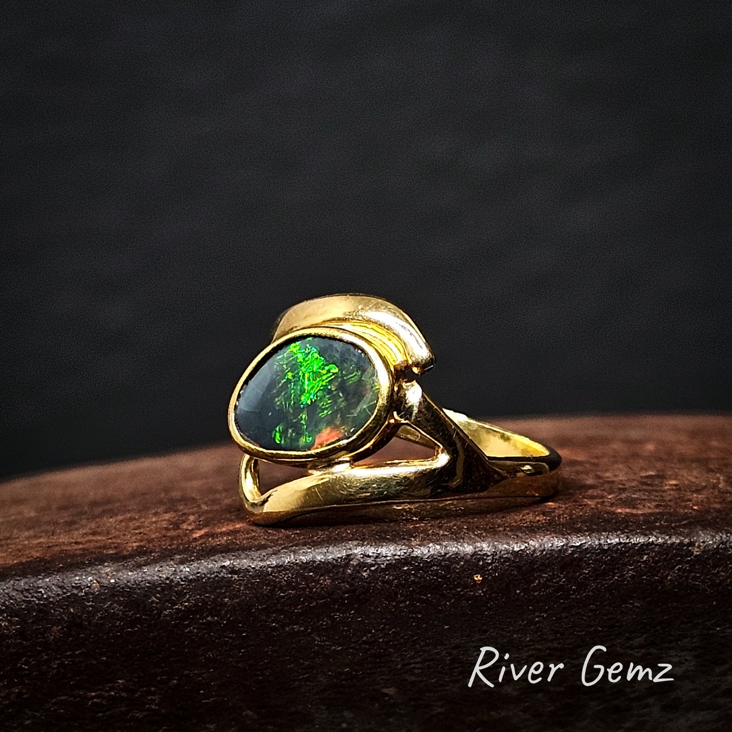 Gold ring with a green free-form cut black on a dark background, featuring the brand 'River Gemz'.